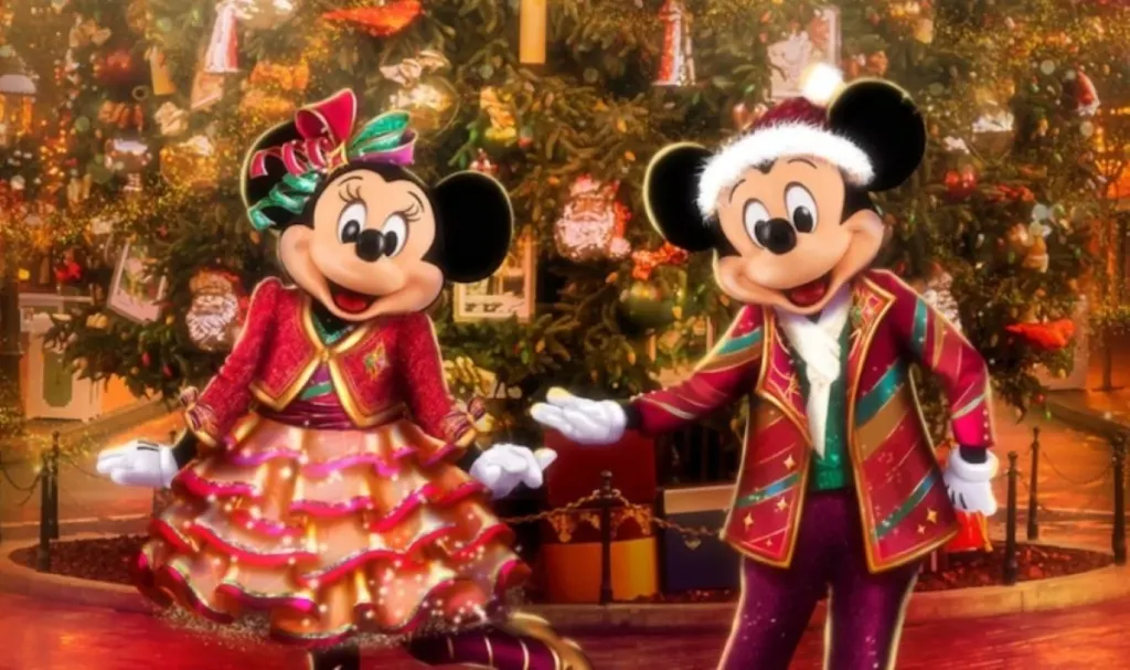 Minnie y Mickey Mouse vestidos con trajes navideños frente a un árbol de navidad decorado.